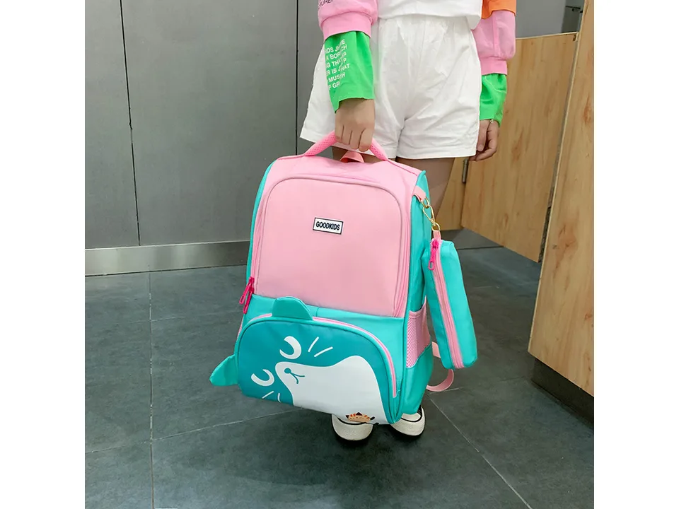 A child holding a pink and teal school backpack with a matching pencil case.