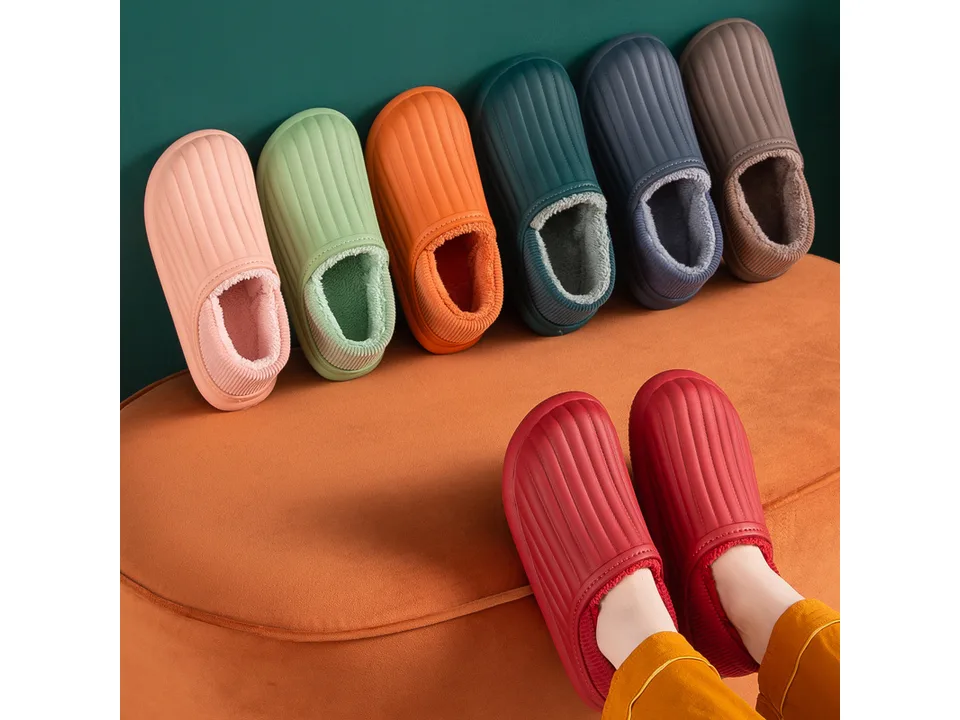 A person wearing red plush thermal slippers with various other colors lined up behind them.