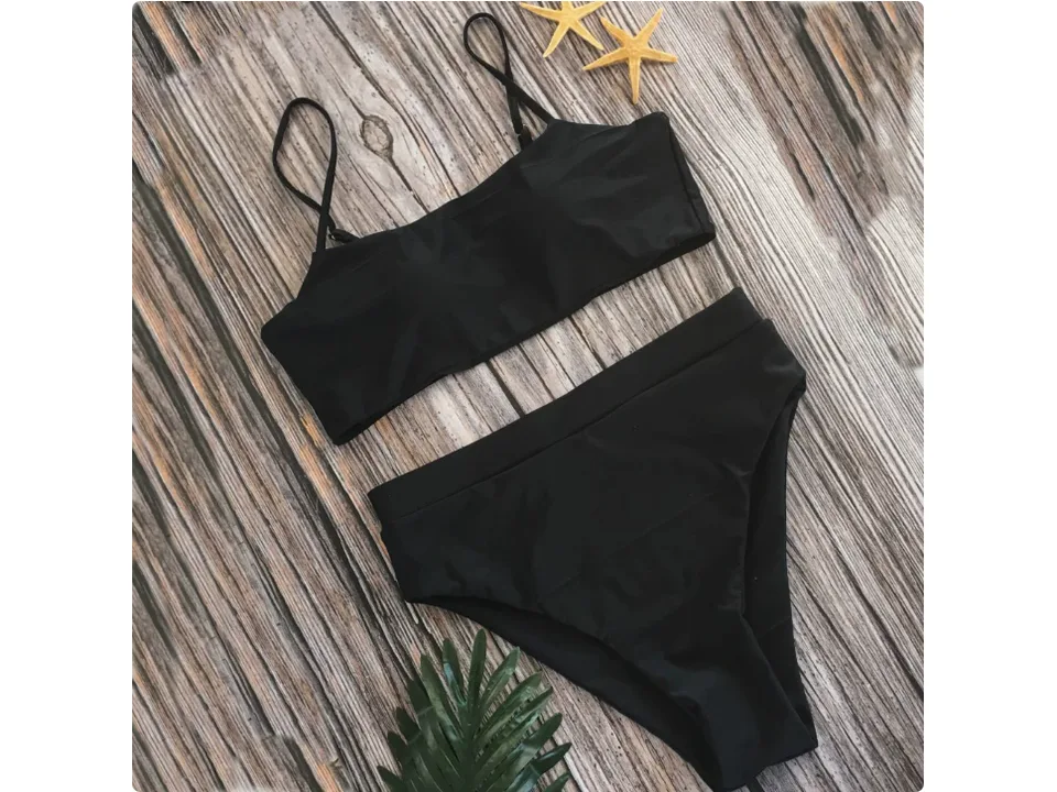 Black bikini set with high-waisted bottoms and spaghetti strap top on a wooden background.