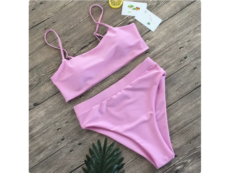 Pink bikini set with high-waisted bottoms and spaghetti strap top on a wooden background.