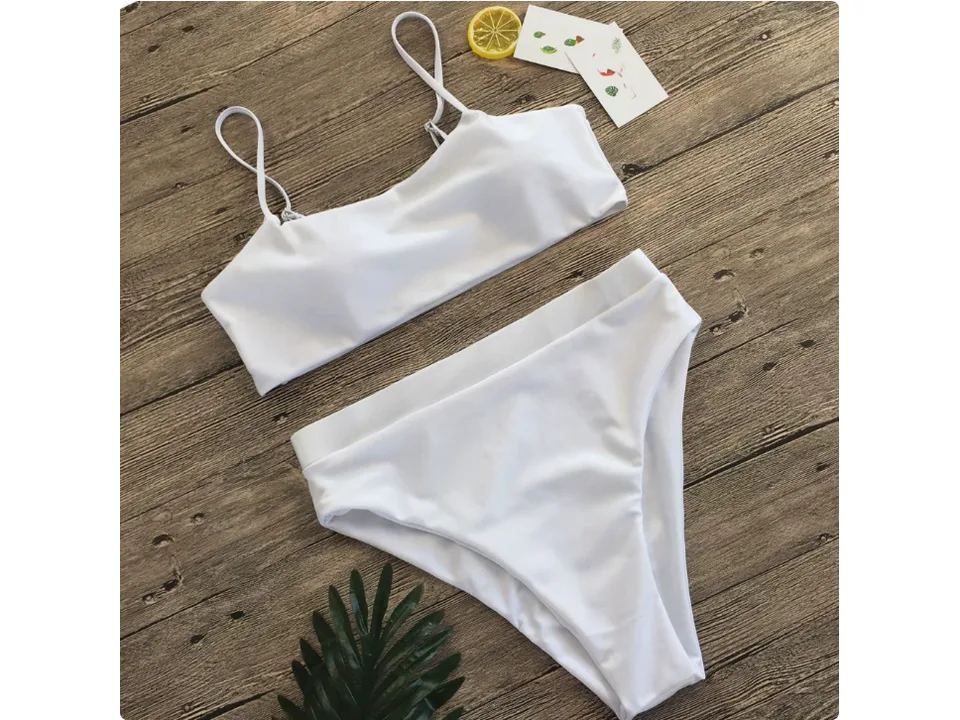 White bikini set with high-waisted bottoms and spaghetti strap top on a wooden background.
