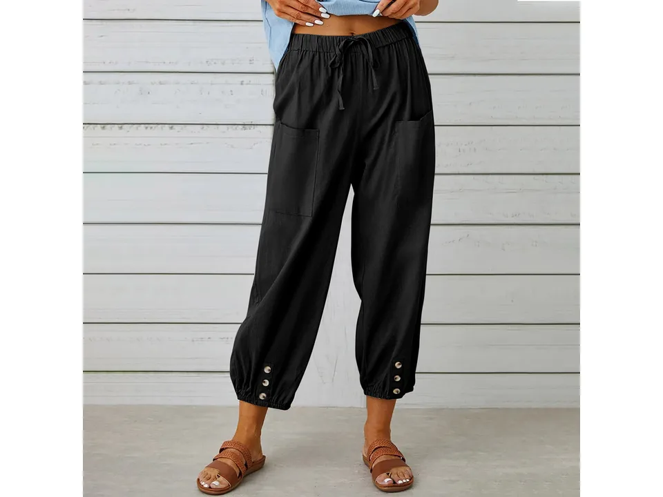 A woman wearing black cropped wide-leg trousers with button details.