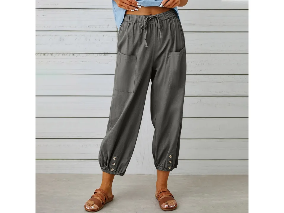 A woman wearing dark grey cropped wide-leg trousers with button details.