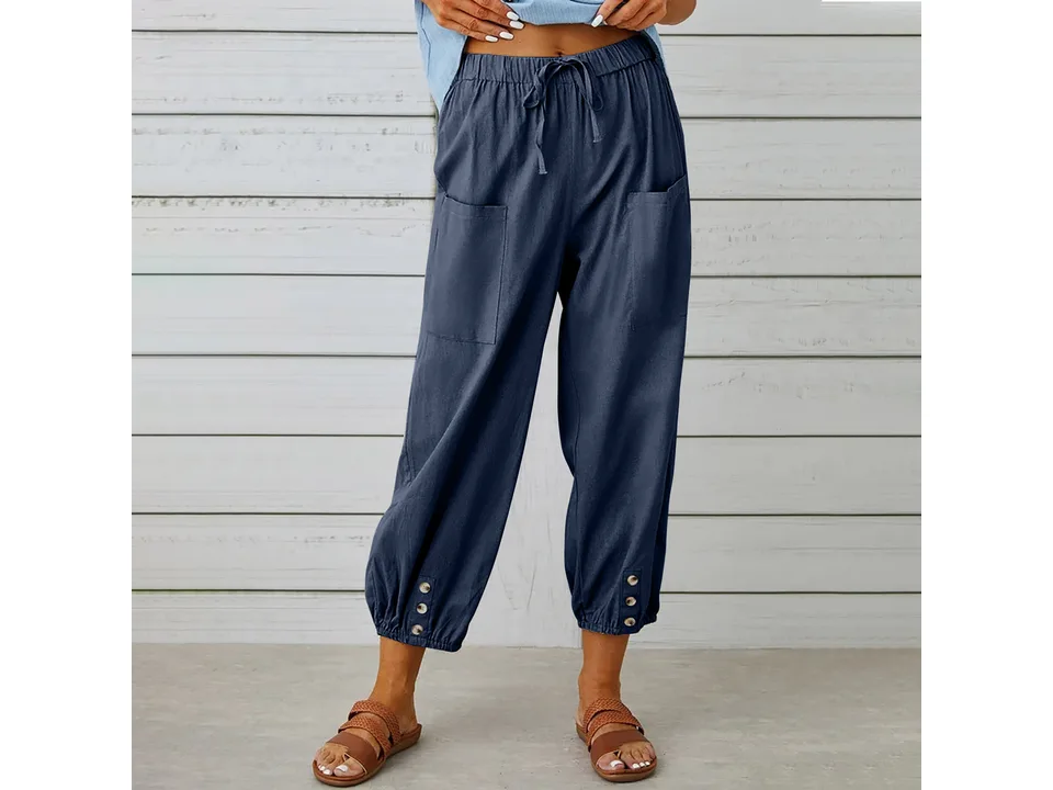 A woman wearing dark blue cropped wide-leg trousers with button details.