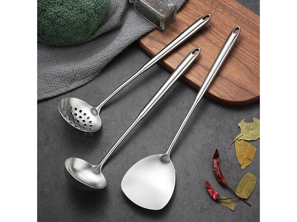 Stainless steel spatula, soup ladle, and colander spoon arranged on a dark surface.