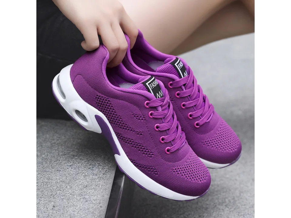 A purple women's athletic sneaker being held by hand.