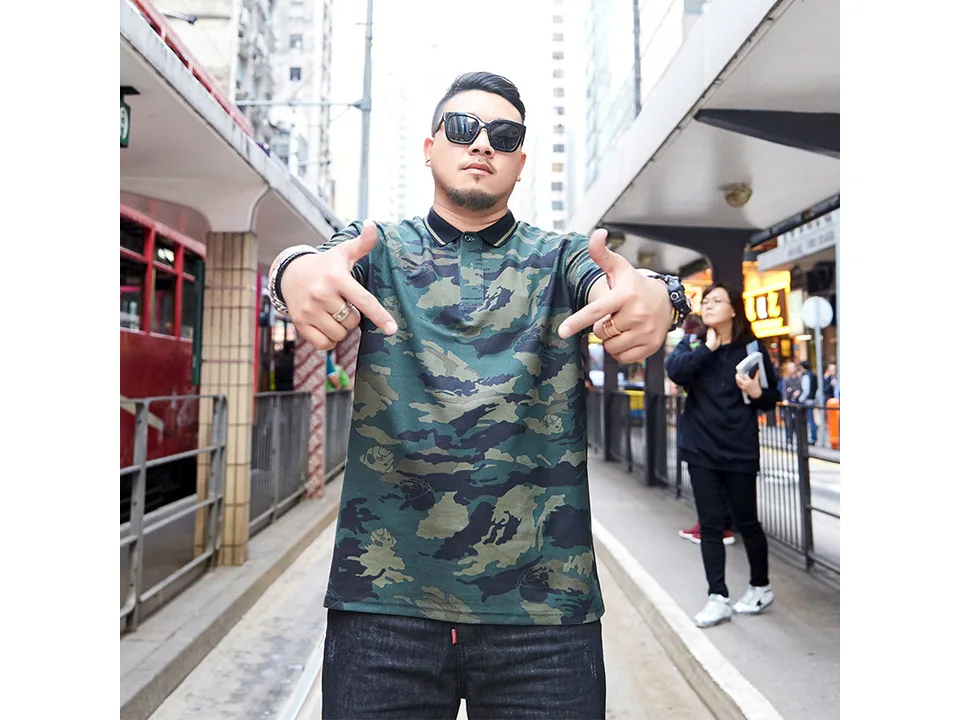 A man standing and wearing a camouflage polo shirt.
