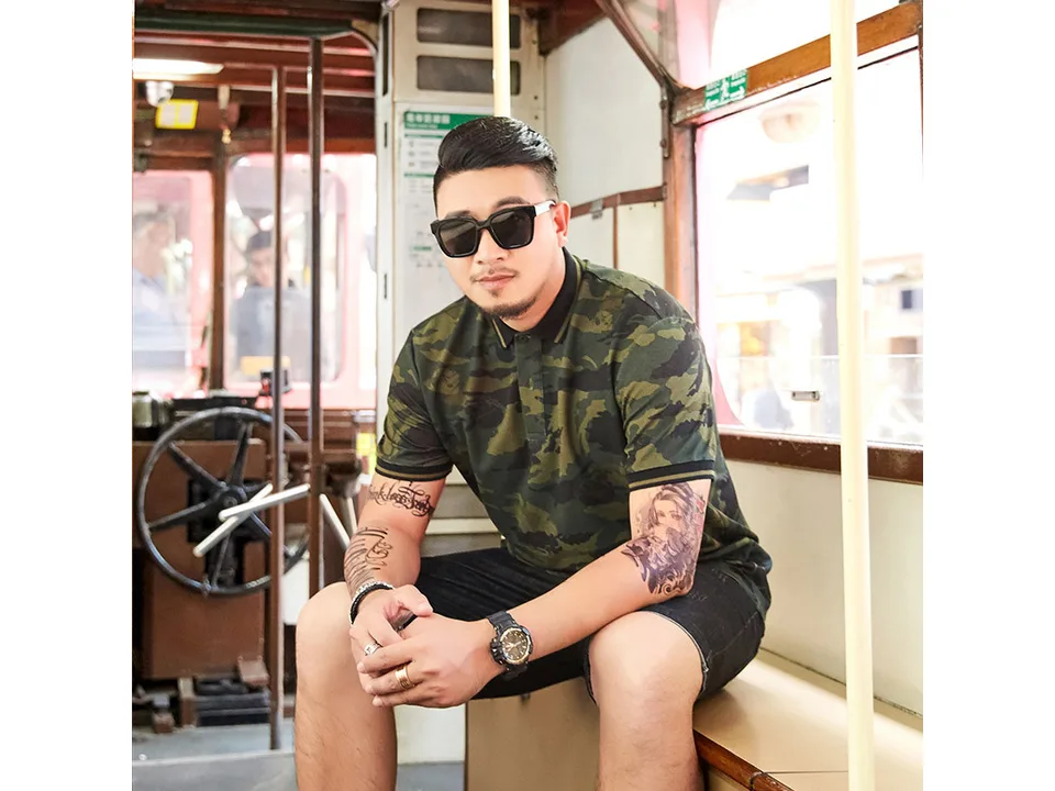 A man wearing a camouflage polo shirt while sitting on a tram.