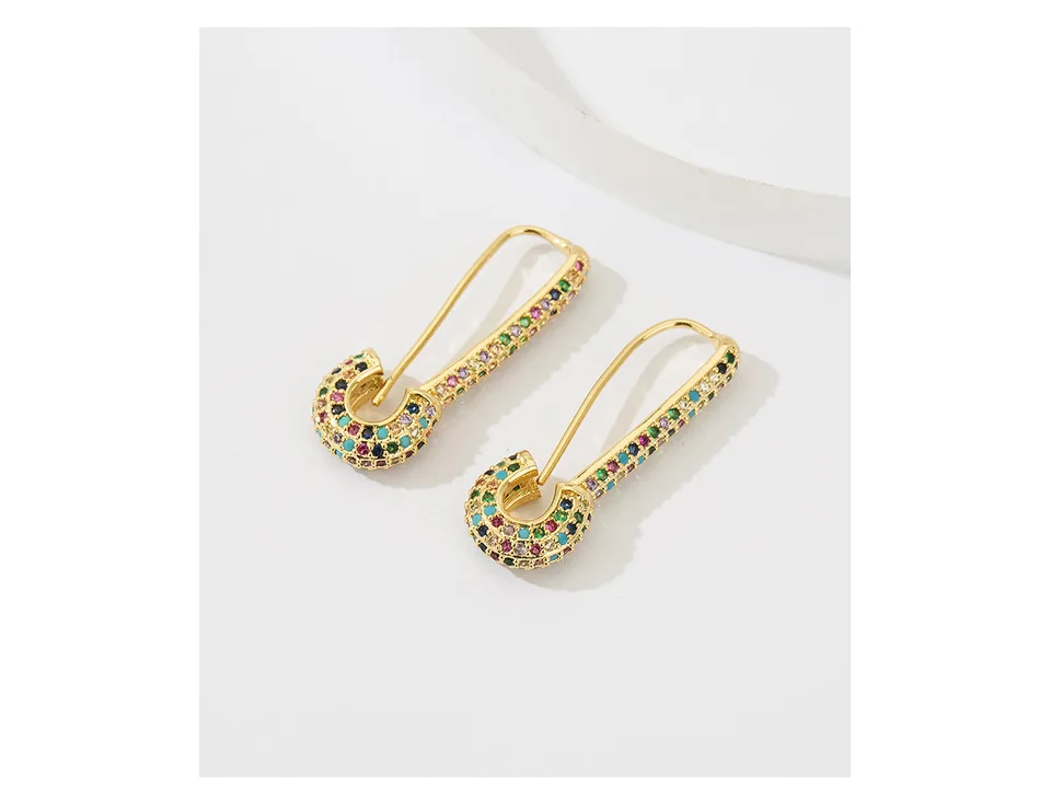Two gold safety pin earrings with multi-colored crystals lying on a white surface.