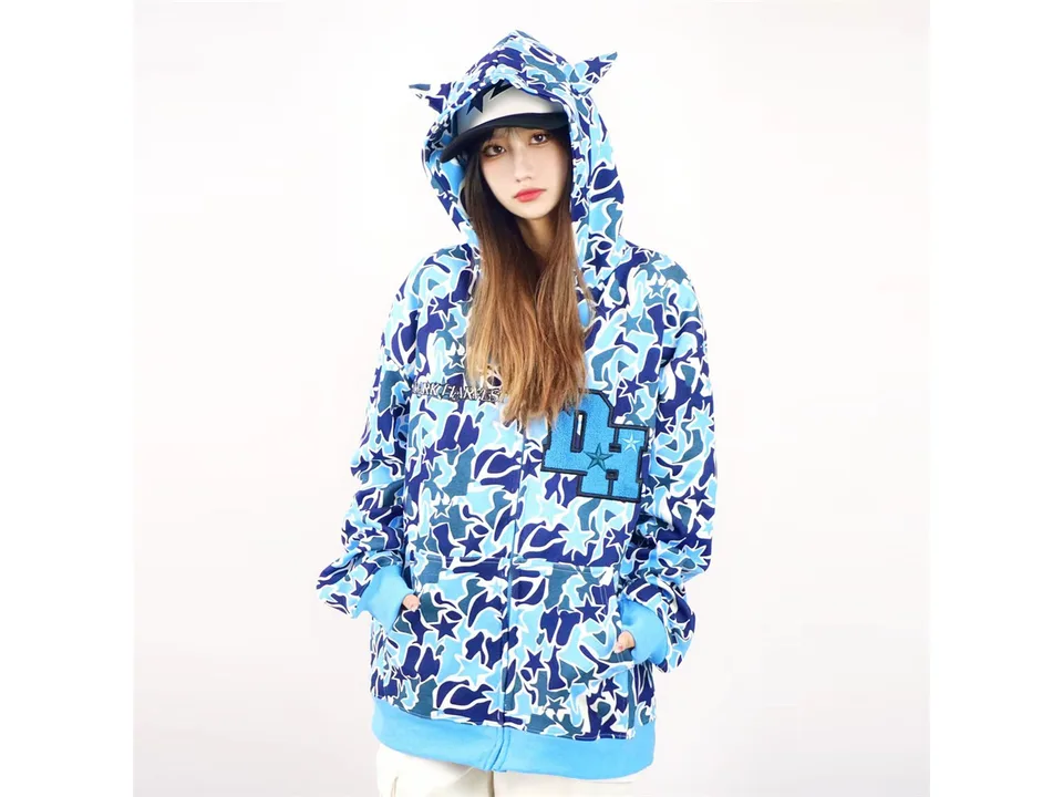 Model wearing a blue camouflage zip-up hoodie with demon horns on the hood.