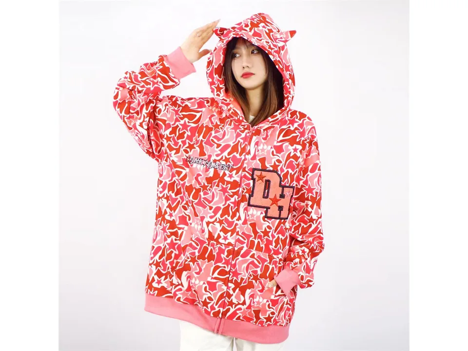 Model wearing a red camouflage zip-up hoodie with demon horns on the hood.