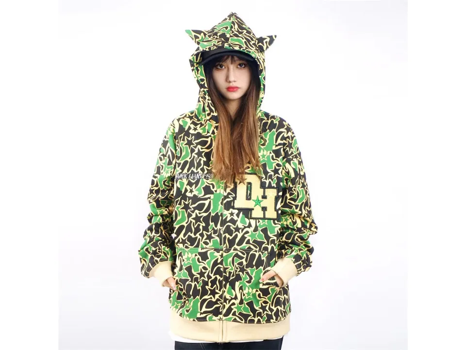 Model wearing a green camouflage zip-up hoodie with demon horns on the hood.