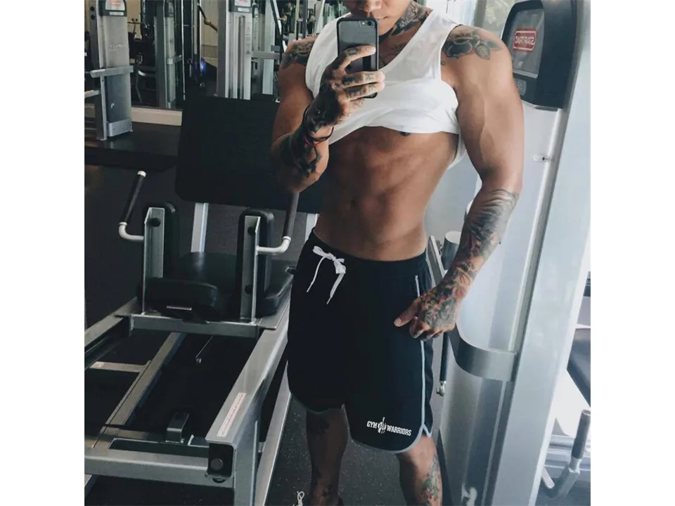 A muscular man wearing black gym shorts in a fitness center.