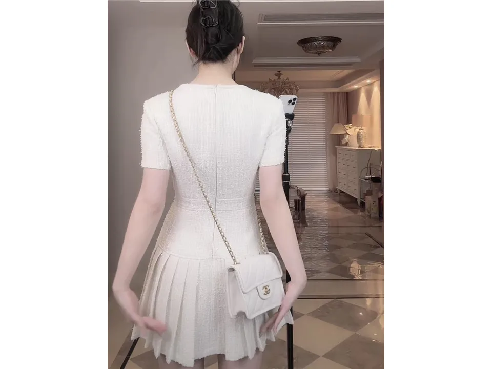 Back view of a woman wearing a white square neck short sleeve pleated mini dress.