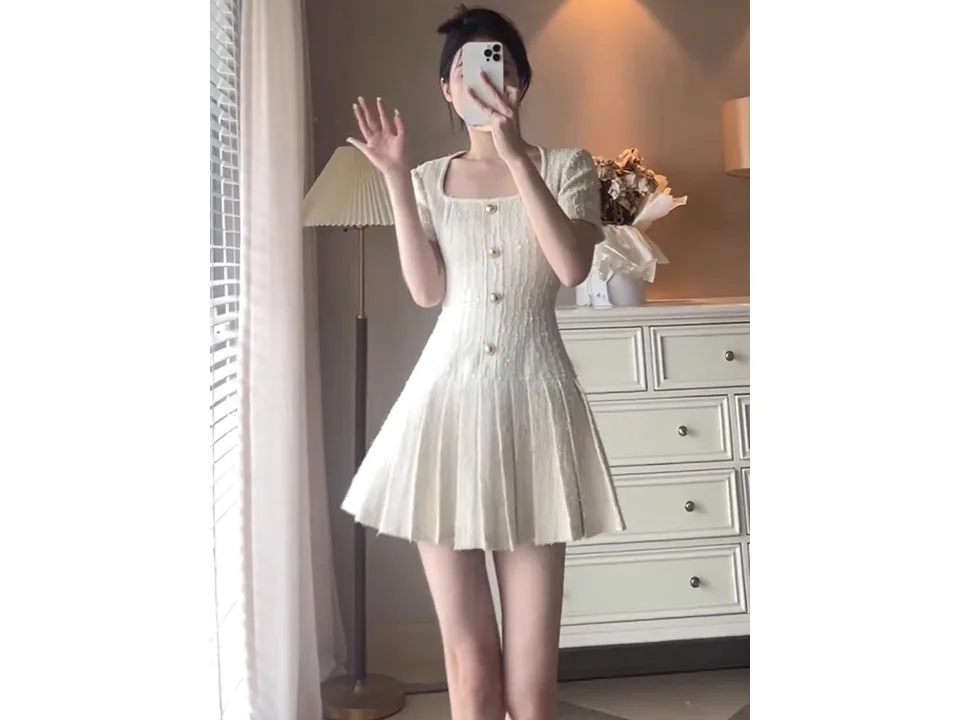 A woman wearing a white square neck short sleeve pleated mini dress.