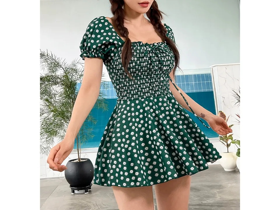 A woman wearing a green floral one-piece swimsuit with short sleeves and a skirt.