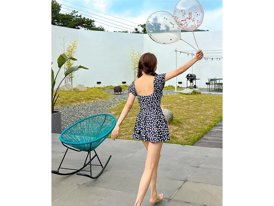 A woman walking away, showing the back view of the green floral one-piece swimsuit.