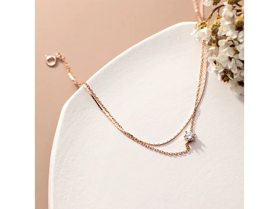 Rose gold double layer anklet with a single cubic zirconia charm on a white plate with flowers.