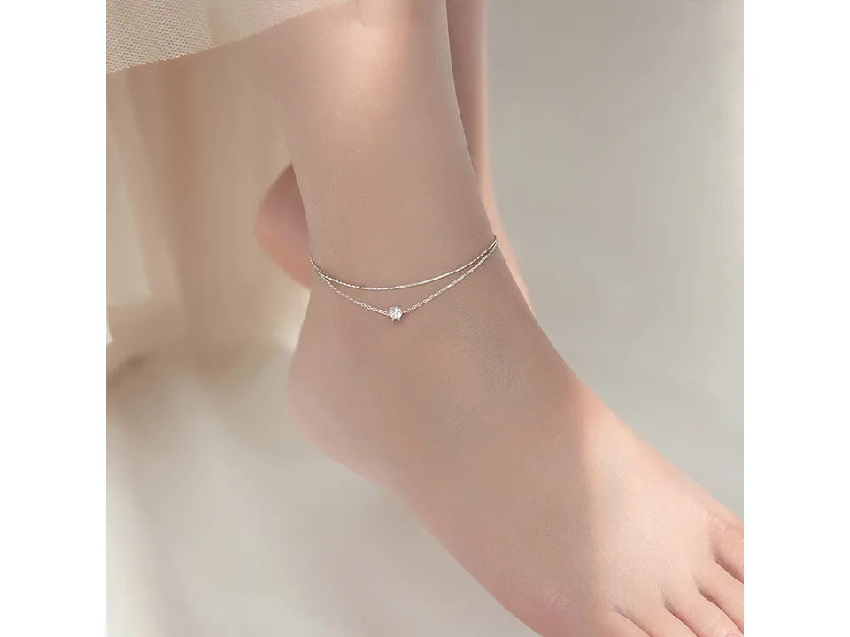 Silver double layer anklet with a single cubic zirconia charm worn on an ankle.