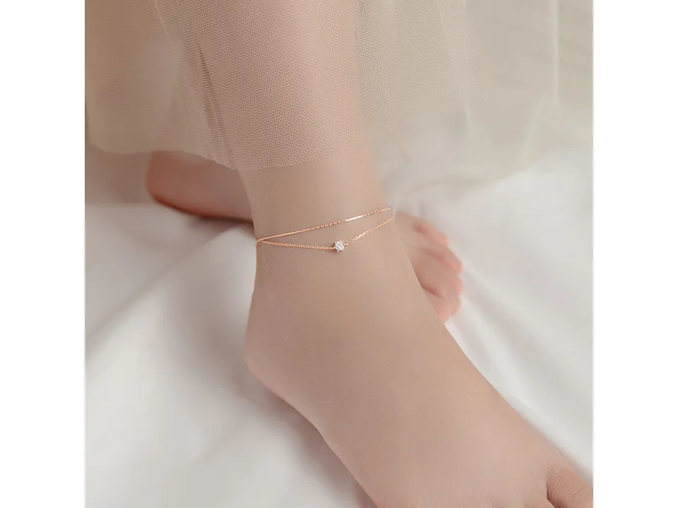 Rose gold double layer anklet with a single cubic zirconia charm worn on an ankle.