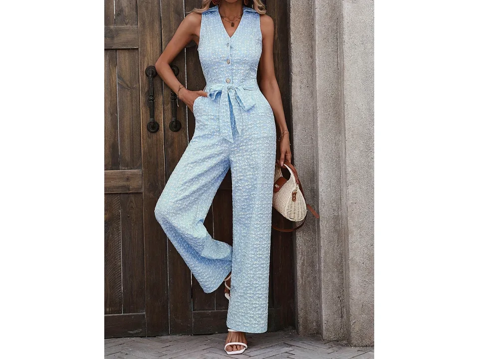 A model posing in a light blue sleeveless jumpsuit against a wooden door.