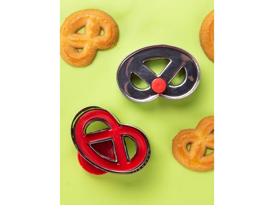 Pretzel-shaped cookie cutters with finished pretzel cookies on a green background.