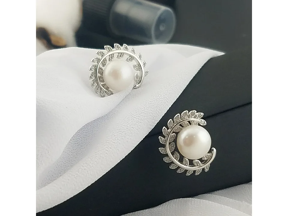 Leaf pearl stud earrings resting on a white cloth and black display box.