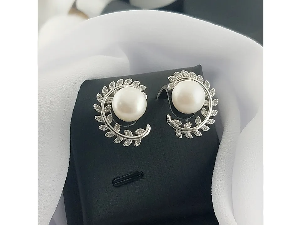 Leaf pearl stud earrings on a black display stand with white fabric.