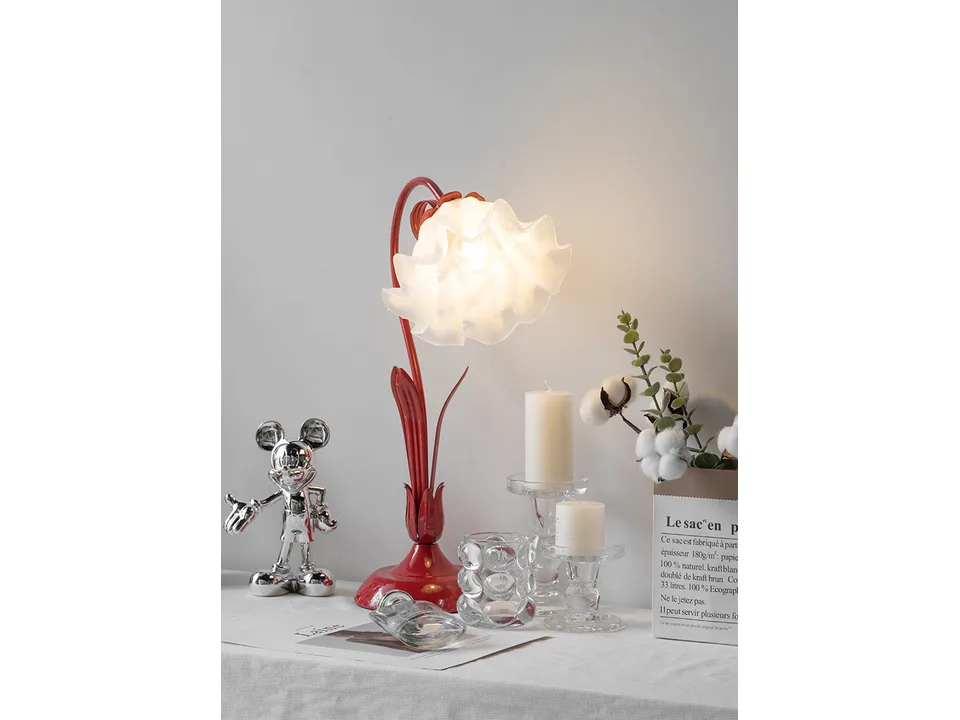 Red flower-shaped table lamp on a table with candles and decor.