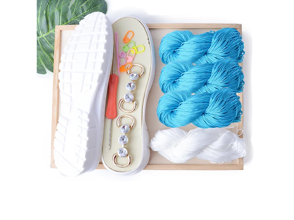 DIY crochet shoe kit with blue yarn, white yarn, shoe sole, crochet hook, and decorative accessories.