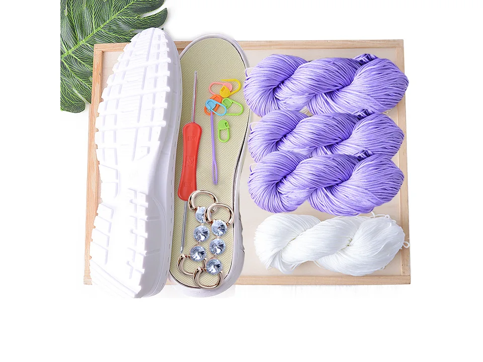 DIY crochet shoe kit with purple yarn, white yarn, shoe sole, crochet hook, and decorative accessories.