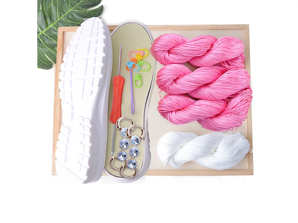 DIY crochet shoe kit with pink yarn, white yarn, shoe sole, crochet hook, and decorative accessories.