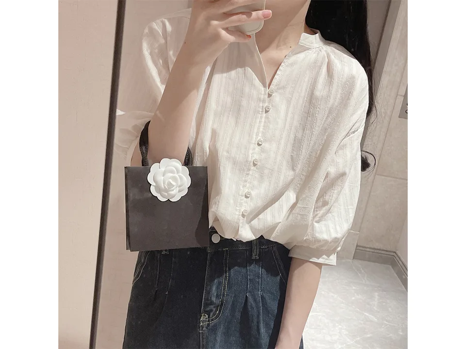 A woman wearing a white button-down shirt with puff sleeves, holding a small black bag.