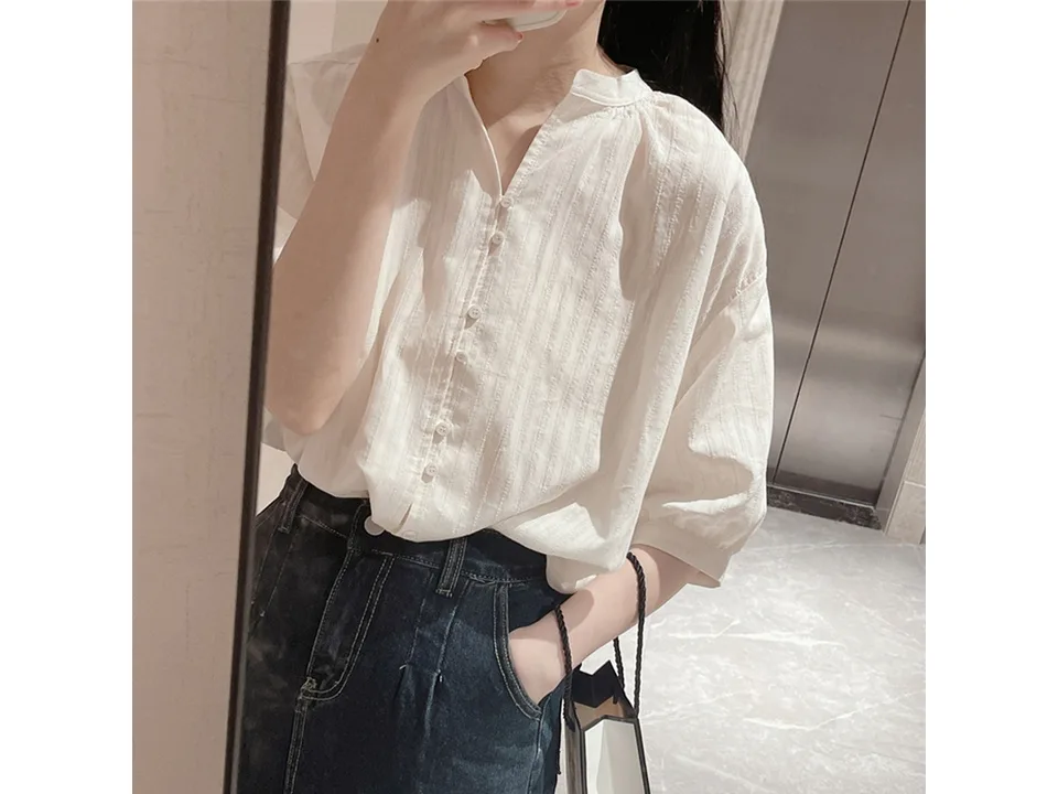 A woman wearing a white button-down shirt with puff sleeves and a mandarin collar.