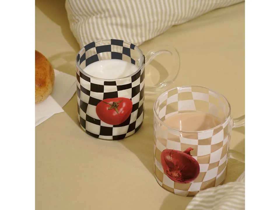 Two checkerboard glass mugs with tomato and onion prints, filled with milk and tea.