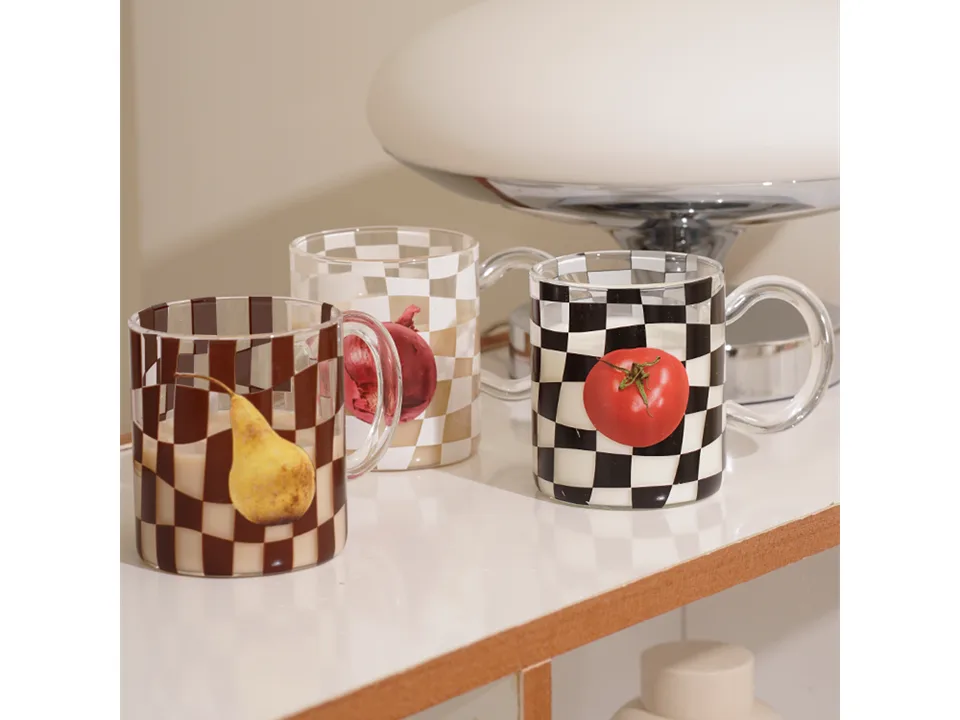 Three glass mugs with checkerboard patterns and fruit prints: a pear, an onion, and a tomato.