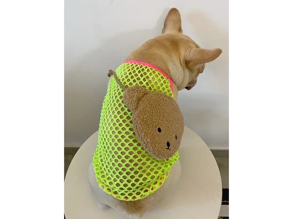 Back view of a French bulldog wearing the neon green mesh vest with a plush bear accessory.