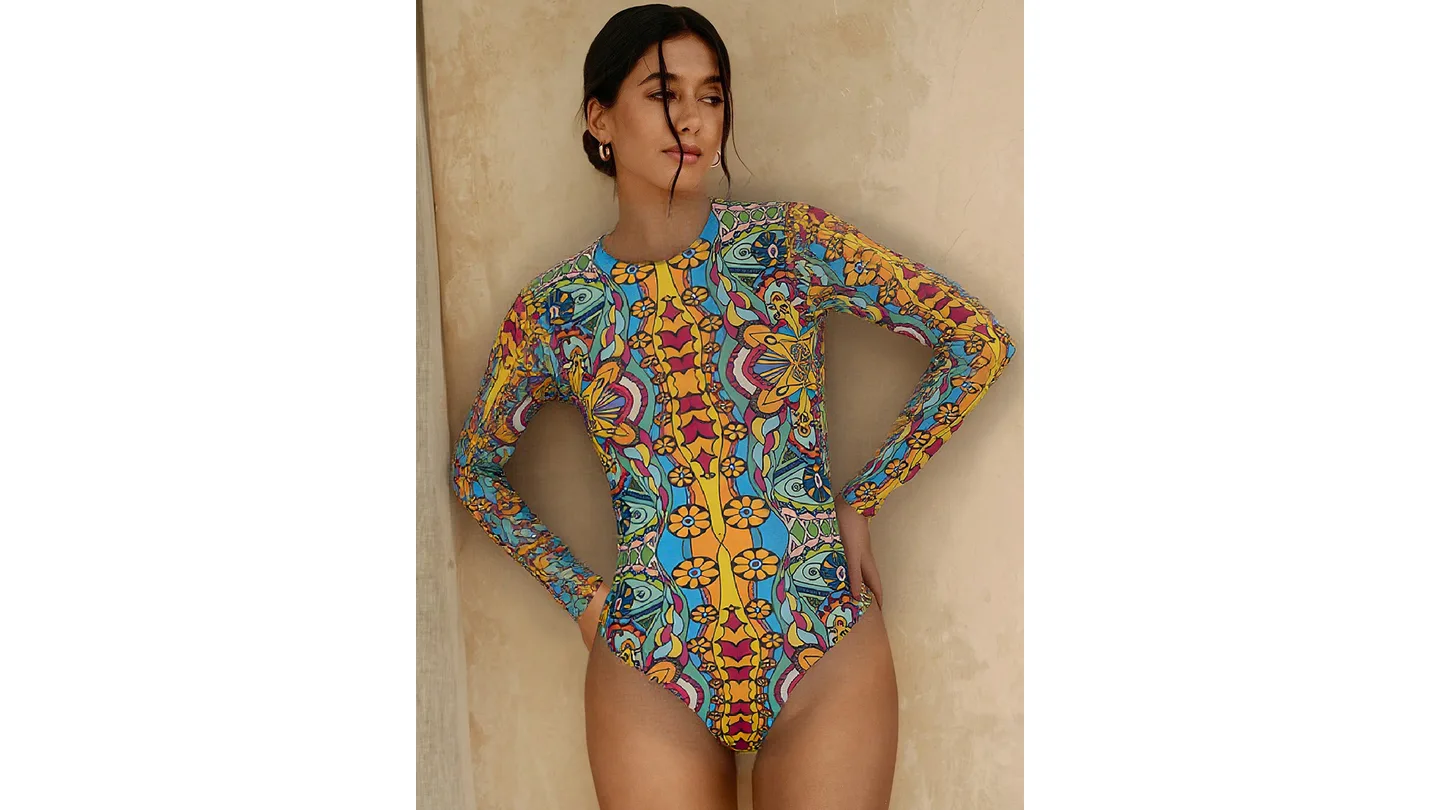 A woman wearing a long-sleeved, colorful patterned one-piece swimsuit.