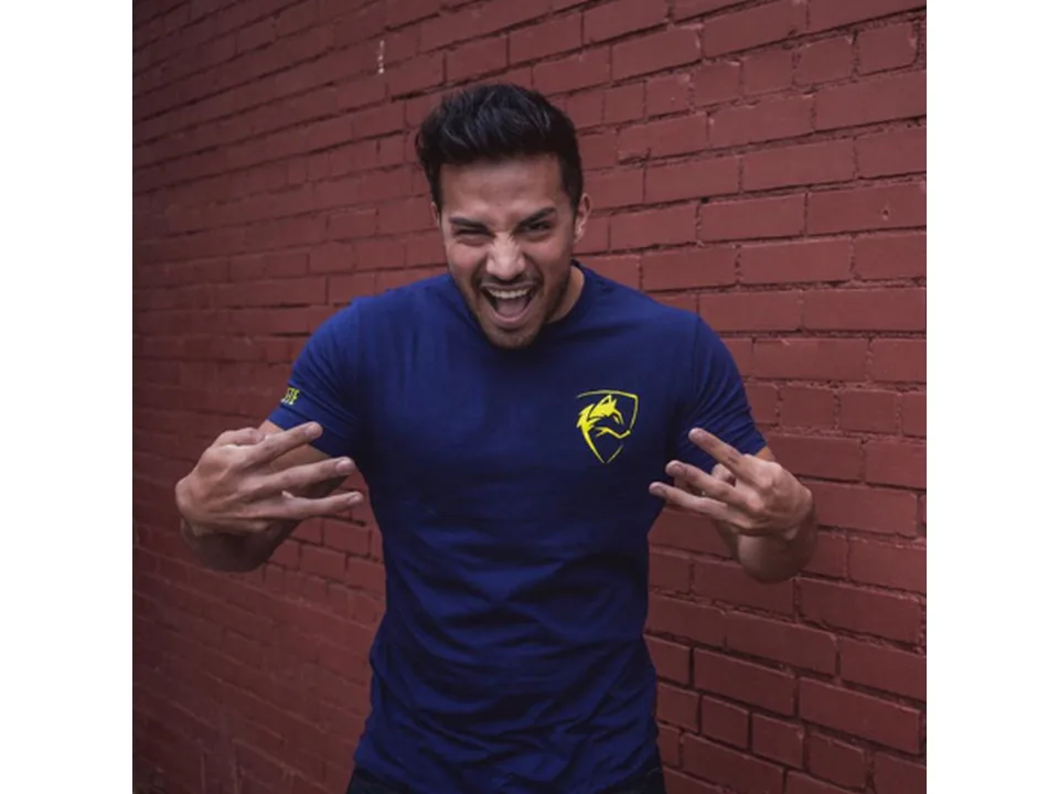 A man wearing a blue slim-fit sports t-shirt with a yellow wolf logo.