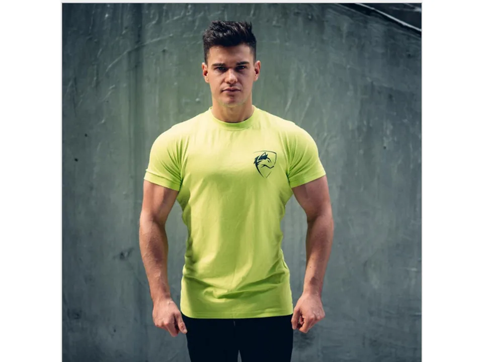 A man wearing a neon green slim-fit sports t-shirt with a black wolf logo.