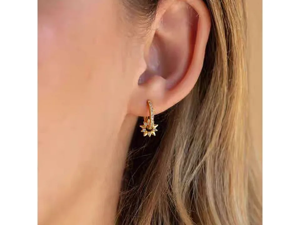 A pair of gold star hoop earrings worn on an ear.
