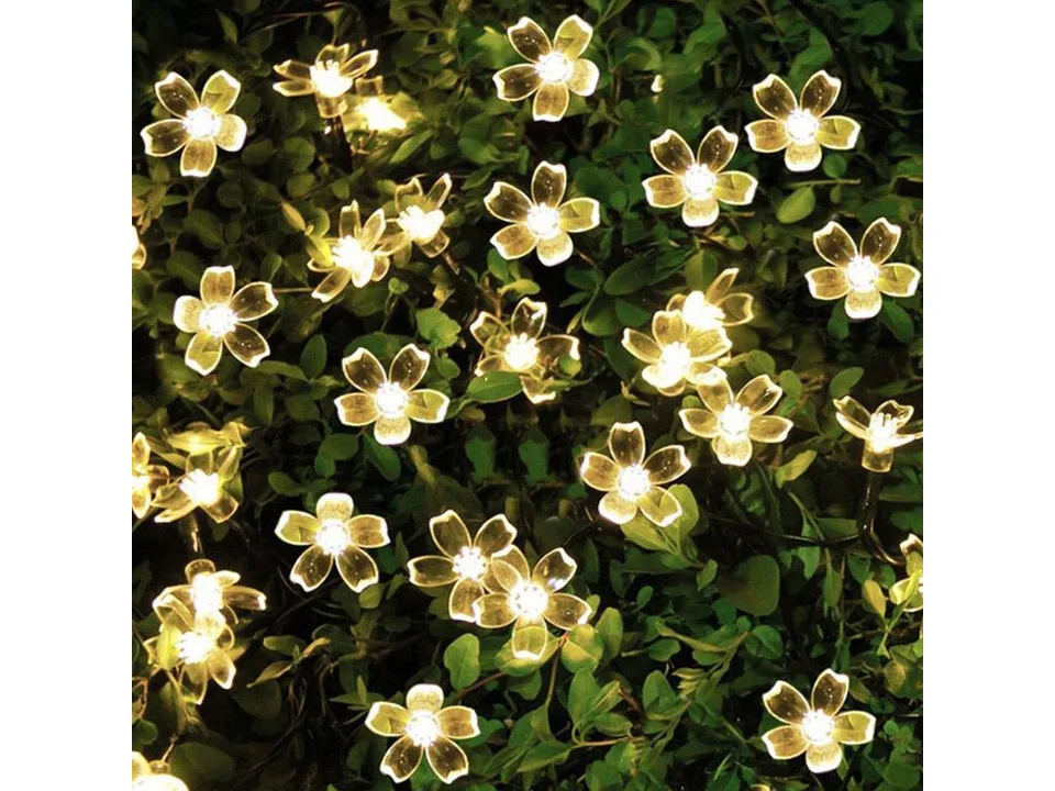 Warm white solar sakura flower string lights on a green bush