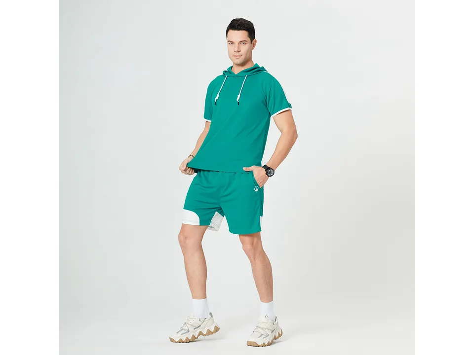 A man wearing a green short-sleeve hooded t-shirt and matching athletic shorts.