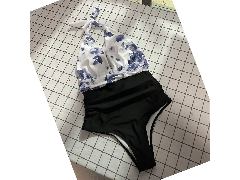 A floral halter top swimsuit with black high-waisted bottoms laid flat on a grid surface.