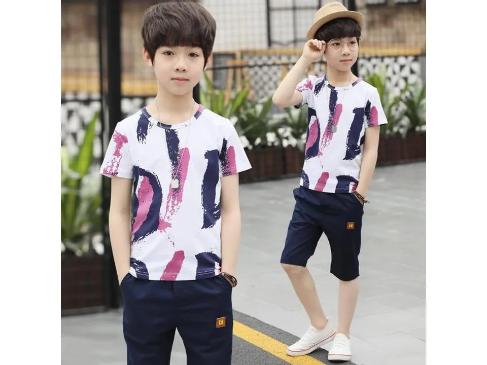 A boy wearing a white t-shirt with abstract patterns and dark blue shorts.