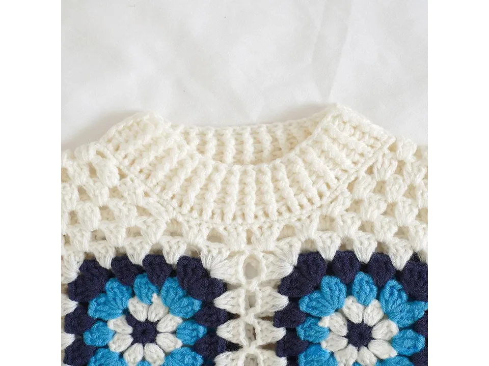 Close-up of the neckline and crochet pattern of the white and blue knitted sweater.