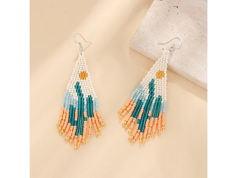 A pair of beaded tassel earrings with a white and blue desert landscape design.