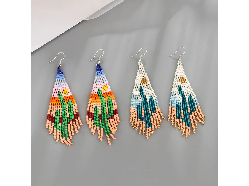 Two pairs of beaded tassel earrings with desert landscape designs on a grey background.