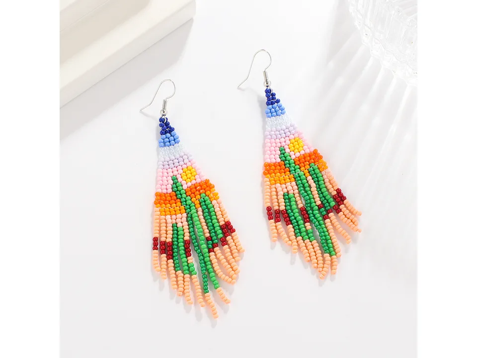 A pair of beaded tassel earrings with a colorful desert landscape design on a white surface.