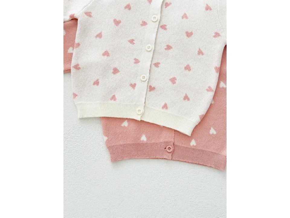 Close-up of the front of the cream and pink heart-patterned cardigans showing buttons and knit texture.
